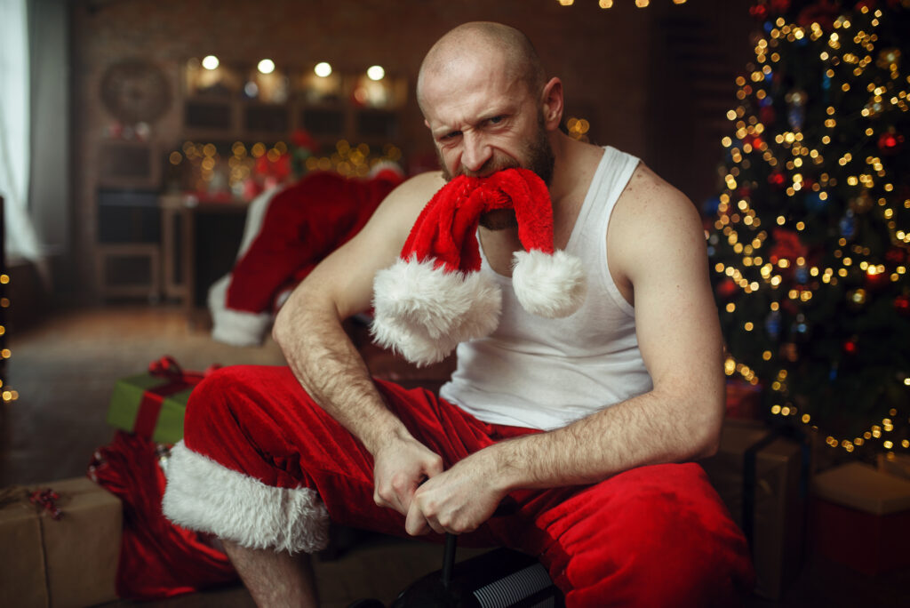 Ein kahlköpfiger Mann im Weihnachtsmann-Outfit sitzt auf dem Boden.